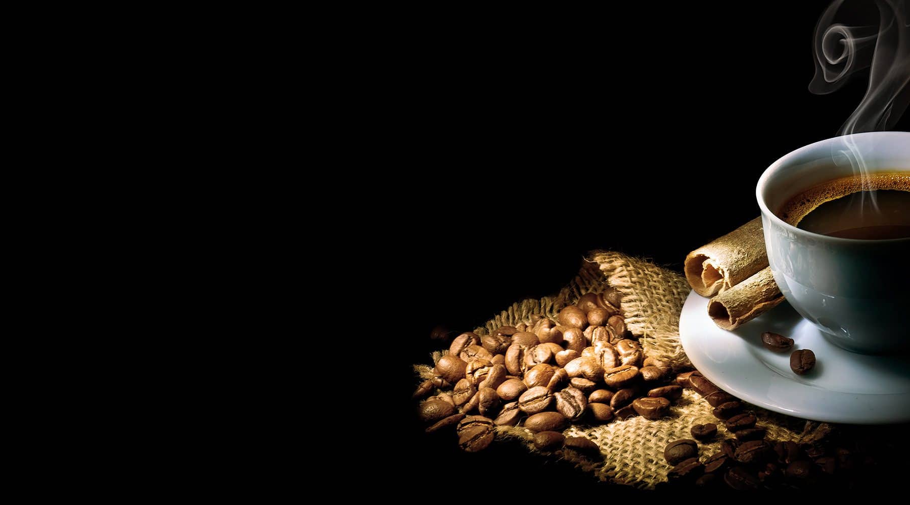 Steaming cup of coffee beside roasted beans