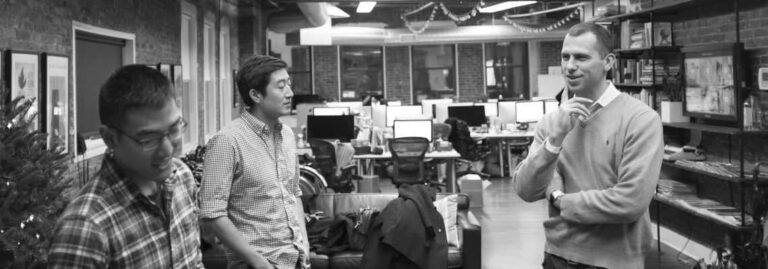 Three colleagues talking beside desks in an open studio office