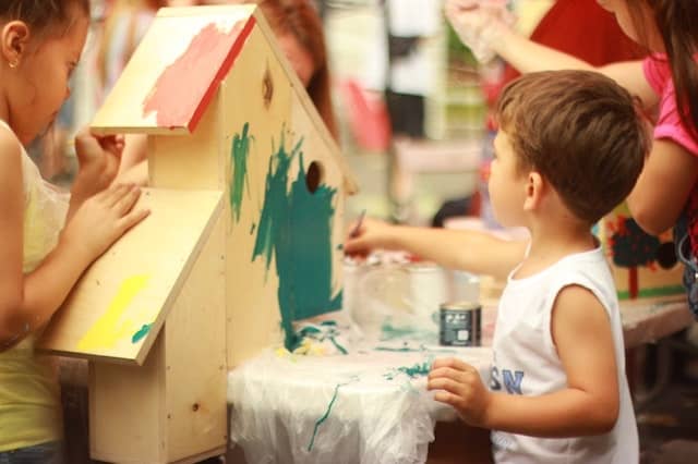 Children painting a wooden playhouse together