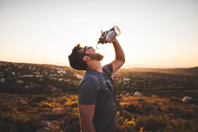 Hiker drinking water on a hillside at sunset