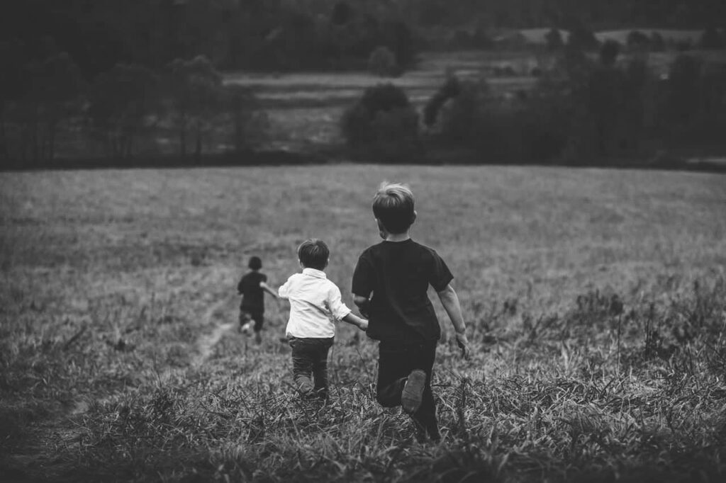 Black and white photograph of three children walking through a field