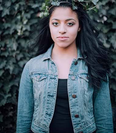Portrait of a woman in a denim jacket against an ivy wall