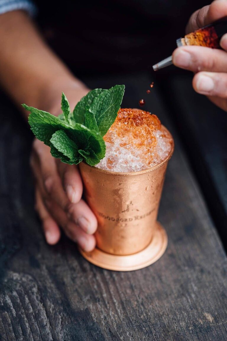 Hands garnishing a copper cocktail mug with mint