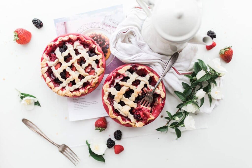 Overhead flat lay of two lattice berry pies with a teapot