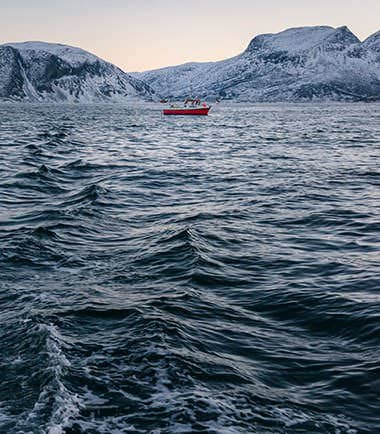 Small red boat on cold open water below snowy mountains