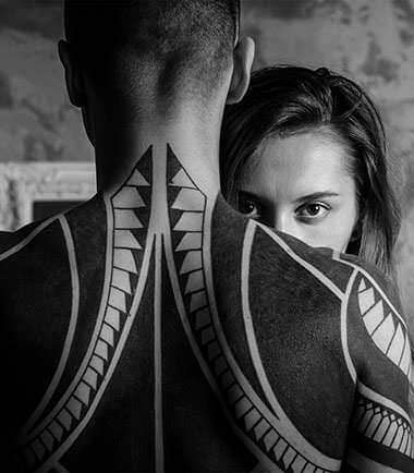 Black and white portrait of a tattooed shoulder and a face behind