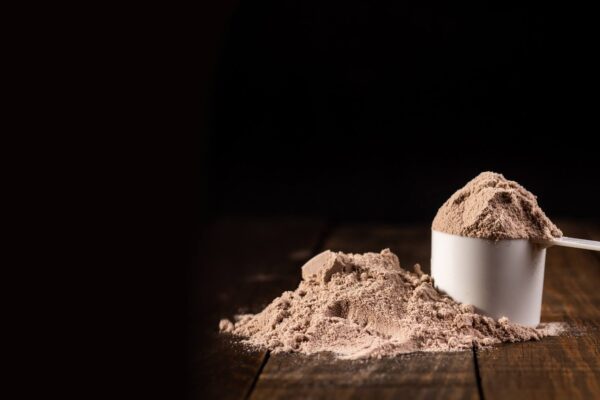 Scoop of whey protein powder on a wooden surface